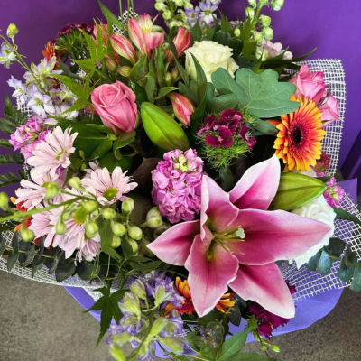 Garden Party Bouquet - A lush, cottage-garden style hand-tied bouquet in soft pinks, mauves and purples with a striking pink lily, roses, daisies, stock and a pop of orange gerbera. Full and abundant — perfect for someone who loves a natural, just-picked look.