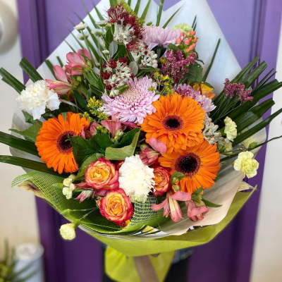Sunset Glow Bouquet - A cheerful bouquet bursting with orange gerberas, lilac chrysanthemums, alstroemeria, carnations and roses among spiky greenery. Warm, sunny and uplifting — guaranteed to brighten anyone's day.