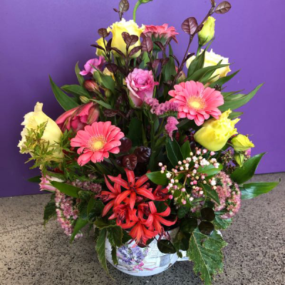Country Garden Pot - A warm, rustic potted arrangement featuring coral gerberas, buttery yellow roses, pink spray roses, fiery nerines and delicate sedum among rich foliage, set in a decorative pot. Full of colour and character — a cheerful gift with real garden charm.